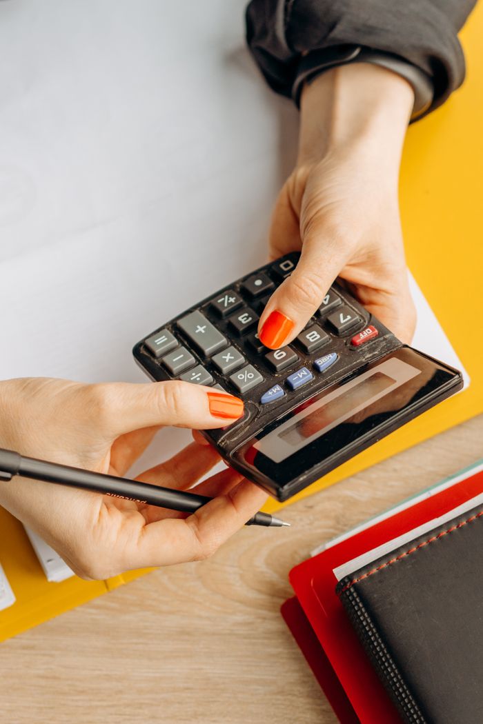 who-we-are Hands using a calculator on a desk surrounded by stationery, embodying business and finance themes.