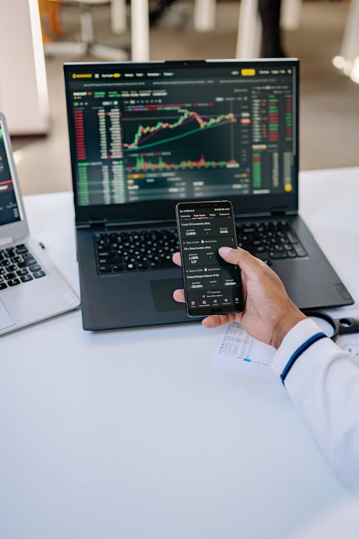 services-03 Person analyzing stock market data on a laptop and smartphone at a desk.